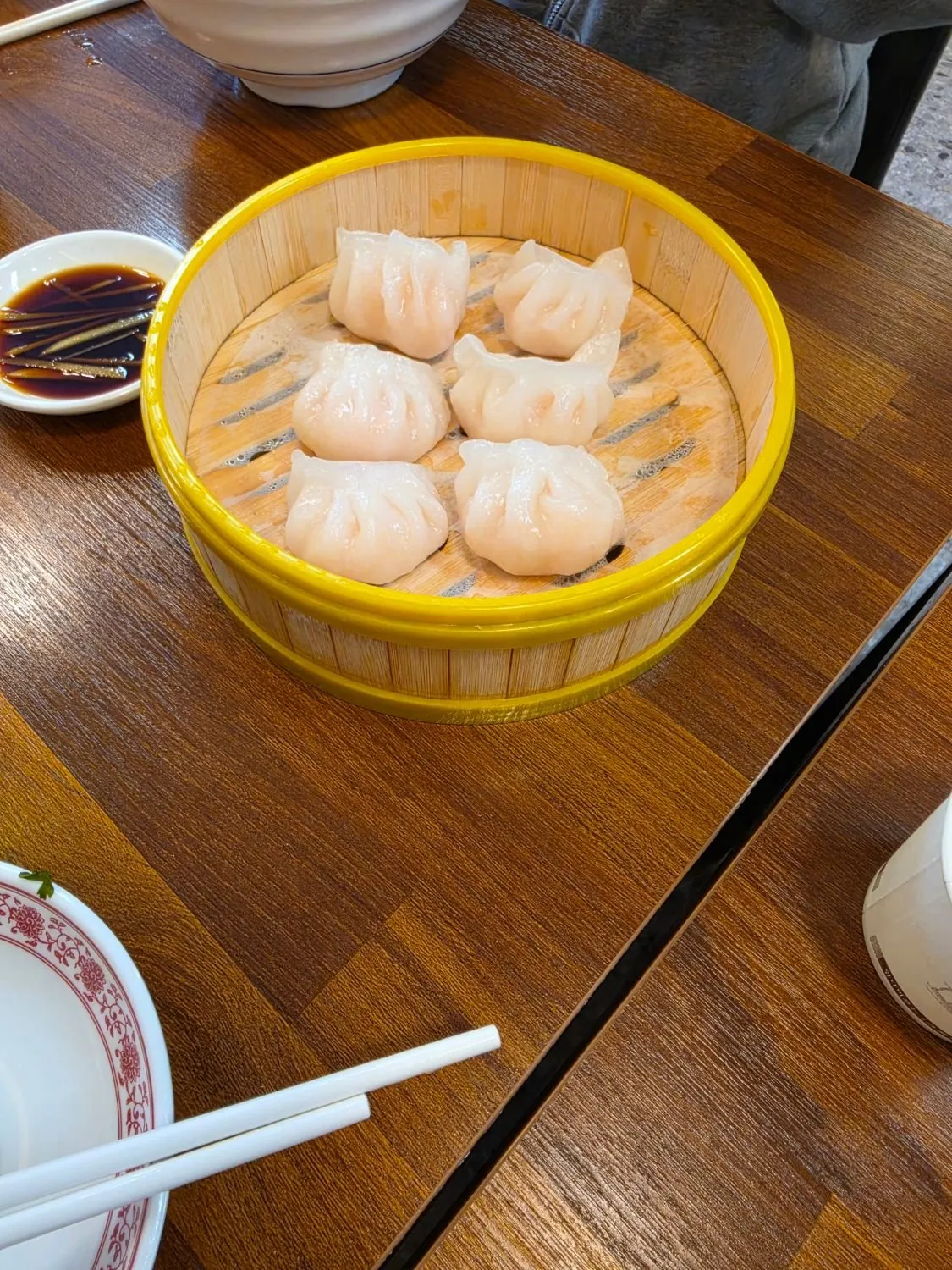 노란 테두리 대나무 찜기 안에 담긴 반투명한 새우만두 여섯 개와 생강채가 들어간 간장 종지